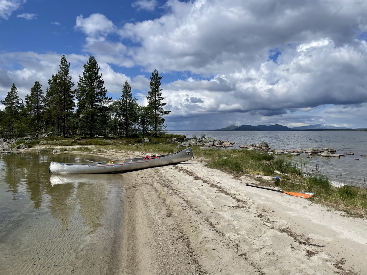Canoe beached on a sandy shore with mountains beyond